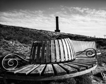 Empty bench on field against sky