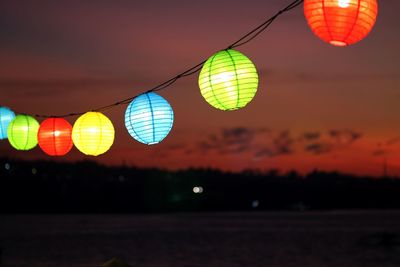 Illuminated colorful lanterns hanging against sky at sunset
