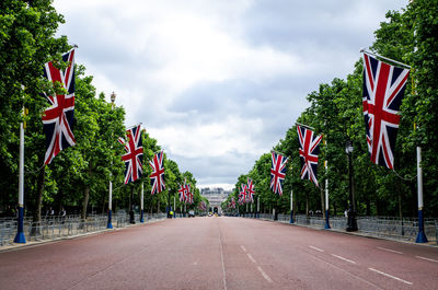 Empty road amidst british flags against cloudy sky