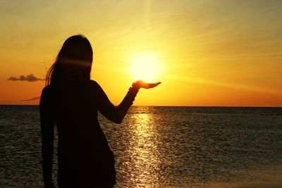 Rear view of silhouette man standing at beach during sunset