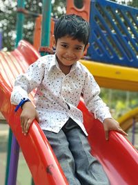 Portrait of happy boy sitting on slide at playground