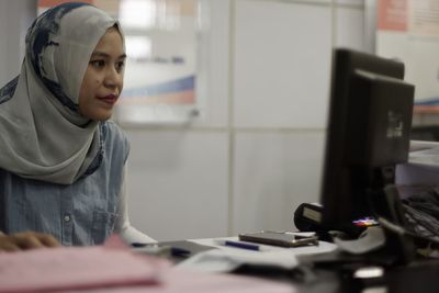 Young woman using computer while sitting at table in office