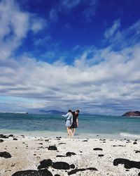 Couple wading in sea against cloudy sky