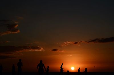 Silhouette people on beach against sky during sunset