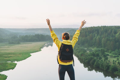 Young woman girl traveler in yellow hoodie with backpack looking at sunrise on beautiful view. local 