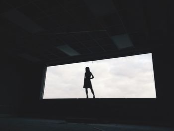 Low angle view of silhouette woman standing on window against sky