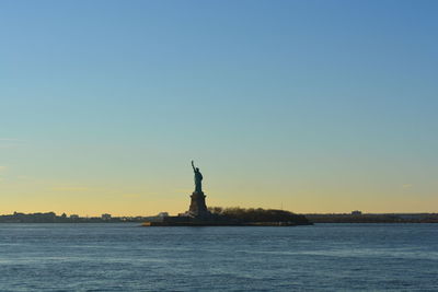 Statue of liberty by hudson river against clear sky during sunset