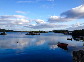 Boats in calm lake against cloudy sky