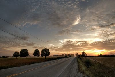 Road by trees against sky during sunset