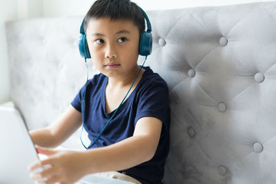 Boy looking away while listening music while sitting on sofa