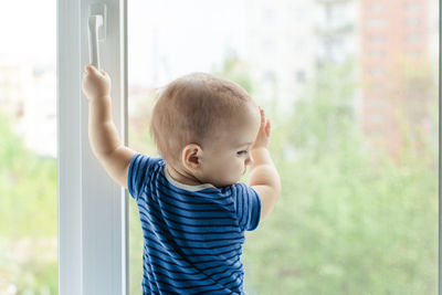 Boy looking away while standing against window