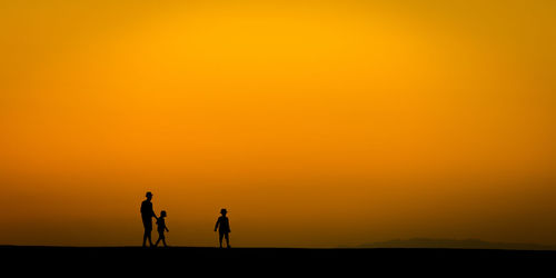 Silhouette people standing by sea against orange sky