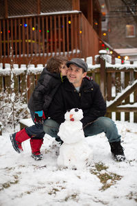 Son kissing his father after they built a snowman in their backyard