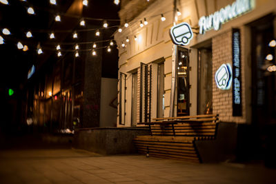 Illuminated lights on footpath by building at night