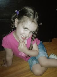 Portrait of cute girl sitting on wooden floor at home