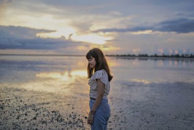 Woman standing at beach against sky during sunset