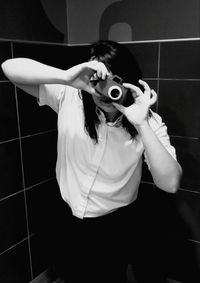 Young woman photographing with camera by tiled wall