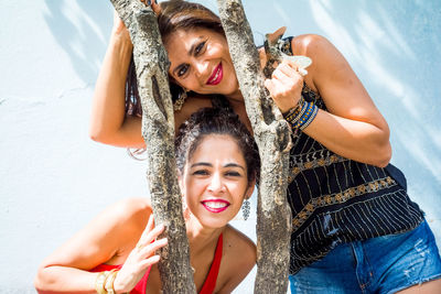 Portrait of two girls between a tree branch against a light blue wall. 