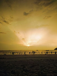 Silhouette people on beach against sky during sunset