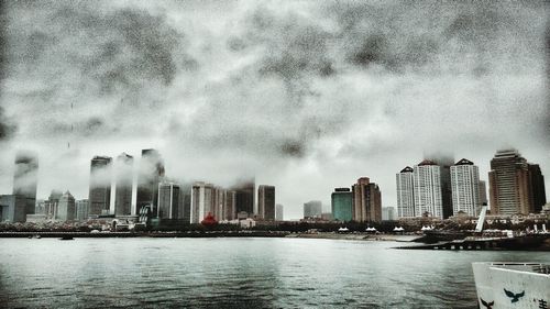 City at waterfront against cloudy sky