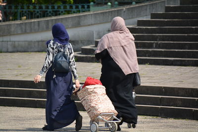 Rear view of muslim women walking with luggage on footpath in city