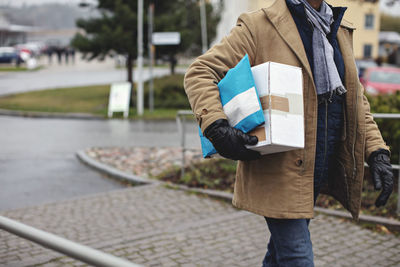 Midsection of senior man with package walking by sidewalk during winter