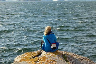 Rear view of woman sitting on rock by sea