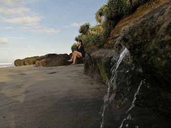 Woman looking at rock formation in water against sky