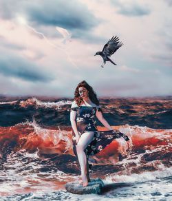 Woman with arms raised against sea against sky