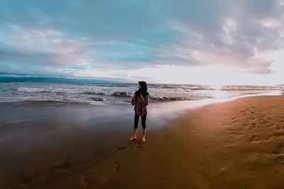 Rear view of woman standing on beach against sky