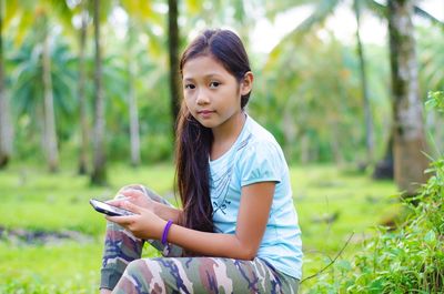 Portrait of girl holding smart phone while sitting outdoors