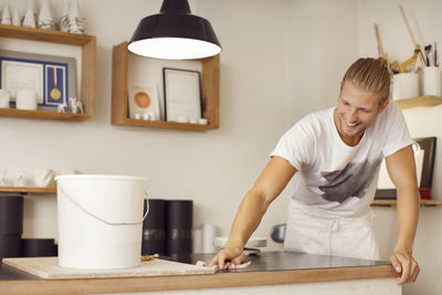 Smiling male worker cleaning table in crockery workshop