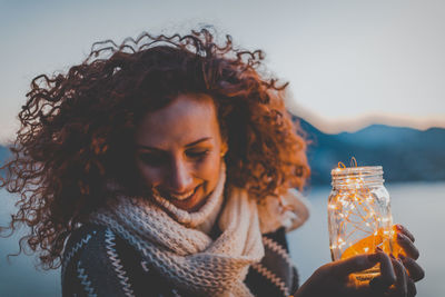 Smiling woman holding illuminated lights against sky