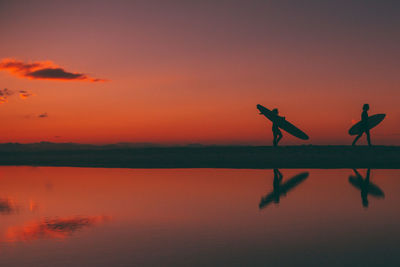 Silhouette people by lake against sky during sunset