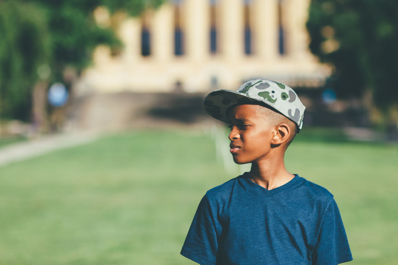 Boy with hat looking away while standing on field