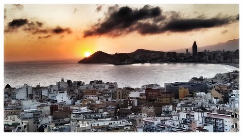 Sea by buildings against sky during sunset