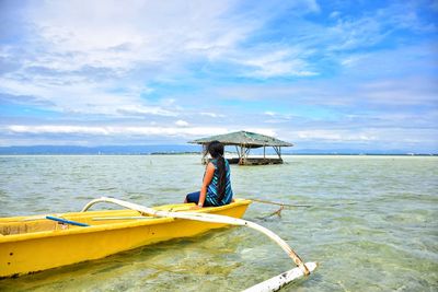 Side view of woman sitting in boat on sea against sky