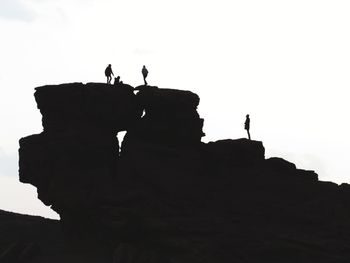 Silhouette people on rock against clear sky