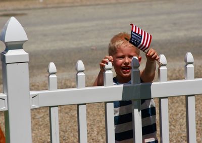 Boy holding small british flag while standing by fence