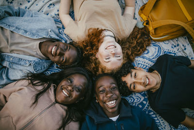 Directly above shot of happy multiracial male and female friends lying down beside each other on picnic blanket