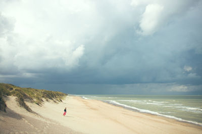 Man standing at beach against cloudy sky