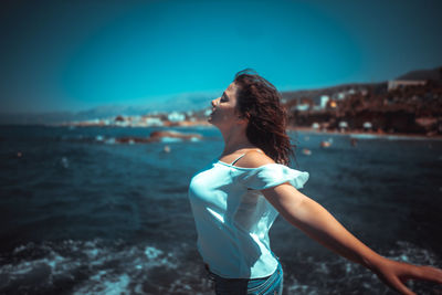 Young woman standing at beach against blue sky