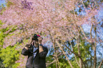 Man photographing through camera while standing against trees