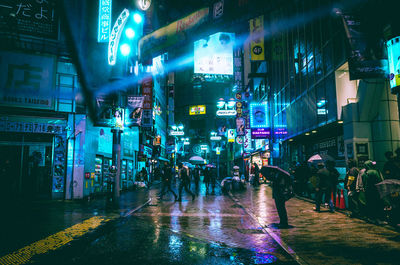 People on illuminated street at night during rainy season