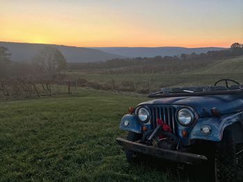 Abandoned car on field against sky at sunset