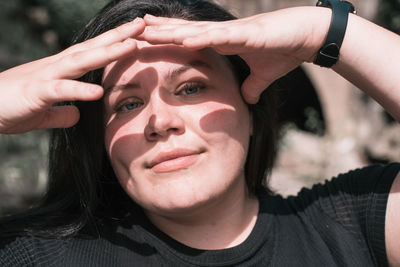 Close-up portrait of a young woman covering eyes from the sun casting shadows on her face