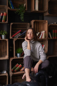 Portrait of woman sitting against shelf