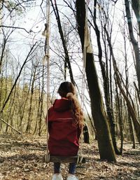 Rear view of woman walking on bare trees in forest