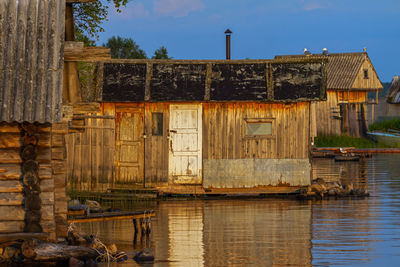 Old wooden house by lake against sky