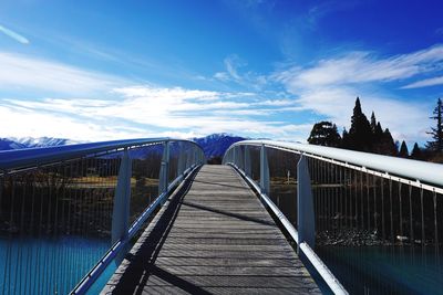 Empty footbridge over lake against blue sky on sunny day